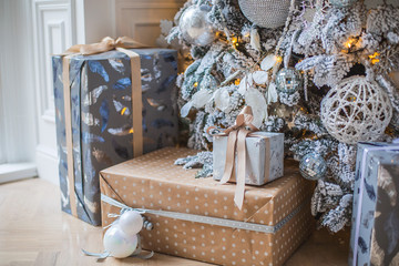 Новогодние подарки лежат под елкой. Заснеженная елка в белых и серебряных тонах