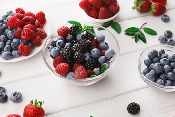 Mixed berries in glass bowls on white wooden table