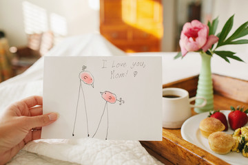 mother holding handmade mother's day card with breakfast in bed
