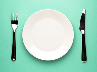 Blank flat plate, knife, fork on a color turquoise table, top view.