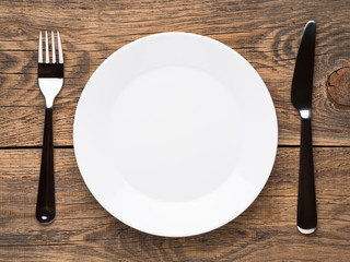 Blank flat plate, knife, fork on a wooden rustic table, top view.