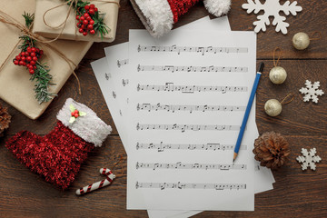 Aerial view of Merry Christmas and music background concept.Essential decorations & ornament with paper white notes.Objects on brown modern rustic table at home studio.Essential items for the season.