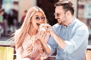 Couple eating and sharing sandwich outdoor.