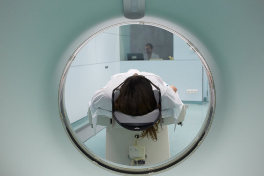 Close up of patient in the CT scan with technician surveying from his control room