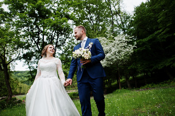 Stunning wedding couple enjoying each other's company in park with blossoming trees on the background.
