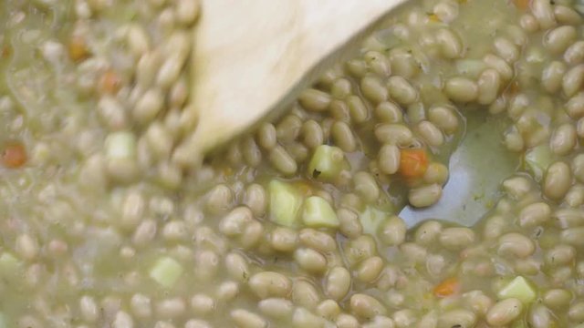 Close video of using a wood spoon to stir hot bean soup in a stainless steel a pan.