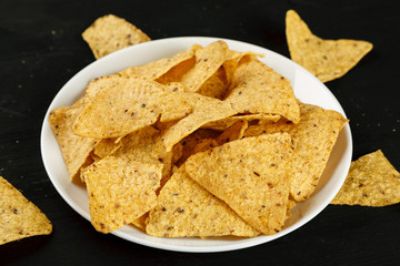 Corn chips nachos in a white plate on a black background