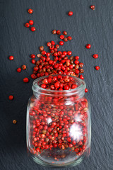 Selective focus Organic Pink Peppercorn in glass jar on black slate stone background