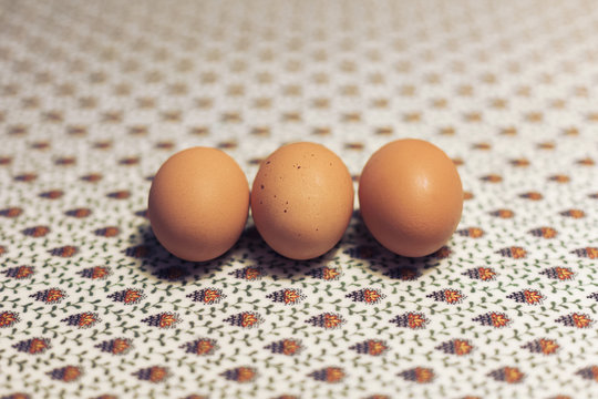 Three eggs in a row on floral patterned oilcloth on table