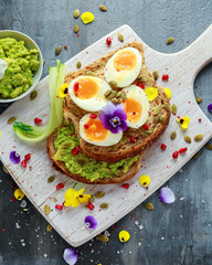 Tasty sandwich with avocado boiled eggs, pumpkin seed and edible viola flowers in a white board. healthy food