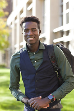 Handsome young black student man smiles standing on college campus with backpack