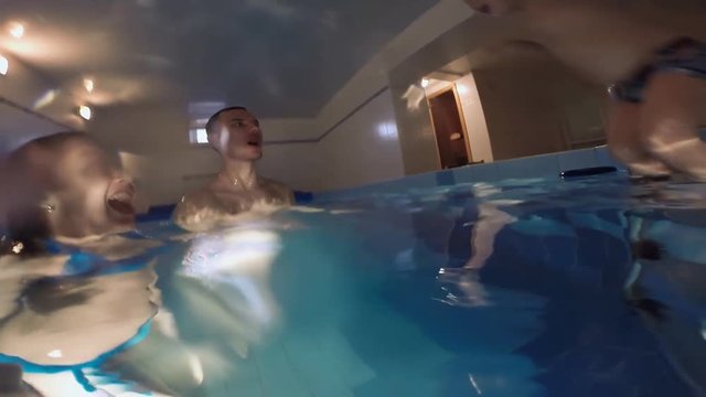The family is swimming in the pool. A small son makes a successful jump from the pool bridge to the parents in the water. Successful joint immersion in the water of the whole family.
