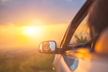 The woman sit in a car on the background of the sunset