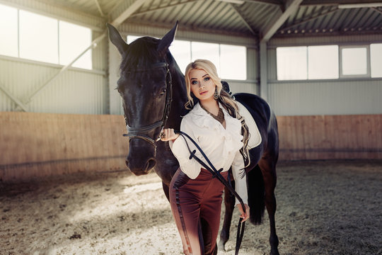 Beautiful elegant young blonde girl standing near her horse dressing uniform competition