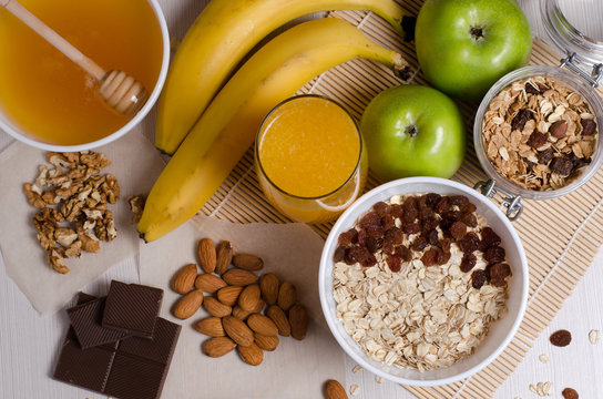 Healthy food. Fruit, homemade granola, nuts, chocolate, oatmeal, honey, orange juice on a white table