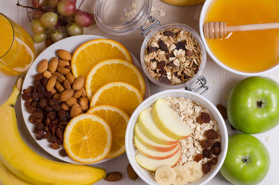 Healthy food. Fruit, homemade granola, nuts, oatmeal, honey, orange juice on a white table