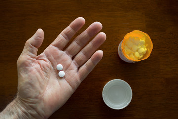 First person POV of a hand holding two round white tablets.