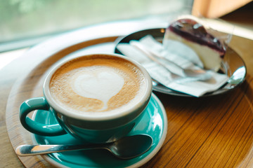 cup with coffee has a heart shape on top placed on wood tray and cake are background. image for coffee art, beverage, drink, food, art concept