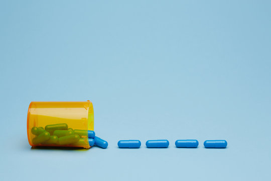 Medicine bottle on side with row of blue capsules