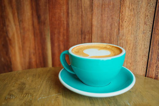 cup with coffee has a heart shape on top placed on wooden table and wood wall are background. image for coffee art, beverage, drink, food, art concept