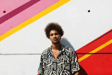 Portrait of a young afro man standing in front of a colourful wall.