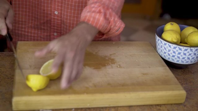 As camera slides from left to right, a chef cuts fresh lemons on a thick wood cutting board.  A juicer stands ready nearby.