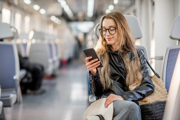 Lifestyle portrait of a young businesswoman sitting with smart phone at the modern train
