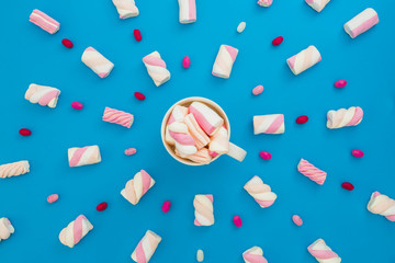 Marshmallow and candy with cappuccino mug on blue background. Flat lay, top view