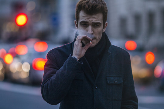 evening city atmosphere,young man smokes a cigar on the city street