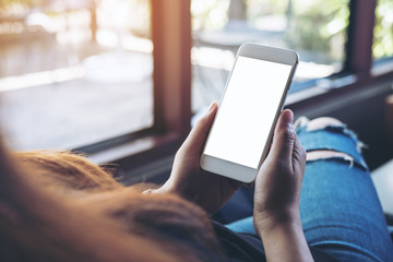 Mockup image of woman's hands holding white mobile phone with blank screen on thigh in cafe