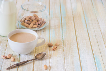 Coffee with milk and pistachios on wooden table, copy space