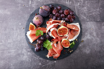 prosciutto with parsley, figs and grapes on a black stone food tray.