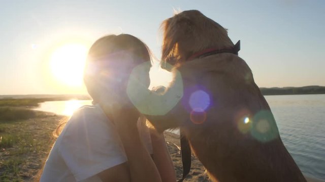 Dog licks teenage girl tongue at sunset.