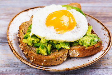 Avocado egg sandwich with whole grain bread on wooden background. Copy space