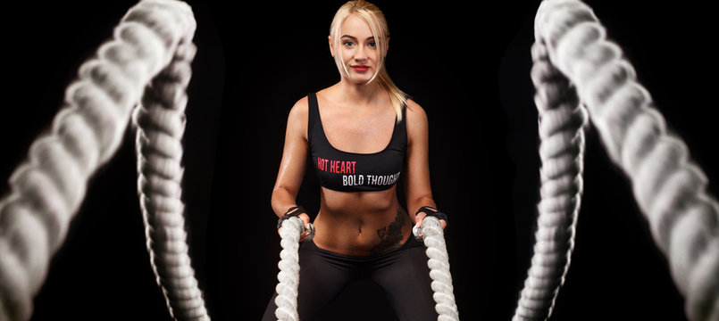 Battle ropes session. Attractive young fit and toned sportswoman working out in functional training gym doing crossfit exercise with battle ropes. Fitness and workout motivation