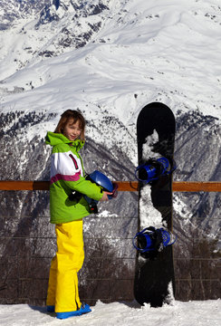 Young snowboarder with helmet in hands and snowboard on viewpoint in winter mountains at sun day