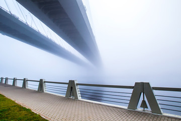 Embankment of the river in the fog. The bridge in the fog. A long bridge over the river.