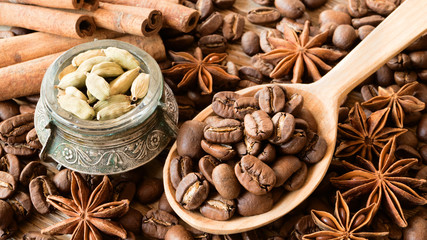 Roasted coffee beans in wooden spoon with anise stars, cinnamon sticks and cardamom in small bowl 