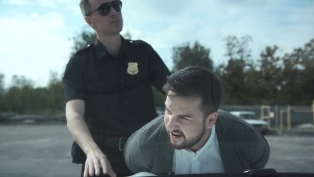 Police Officer Arresting Criminal, Putting Him On Car Trunk And Reading Miranda Rights For Him.