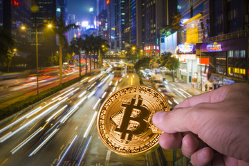 Obraz premium Hand holding a bitcoin with night view of Hong Kong in the background.