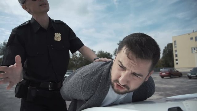 Police officer arresting criminal, putting him on car trunk and reading rights for him.
