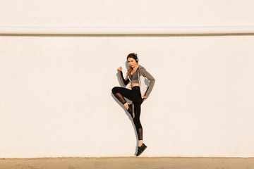 Full length photo of young sport woman jumping near white wall