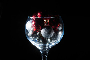 Wine glass filled with Christmas balls. On a black background.