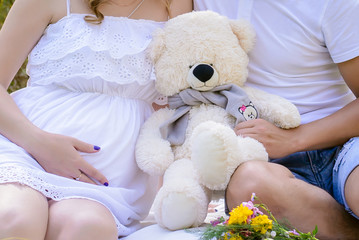 Pregnant couple holding a large teddy bear near the tummy