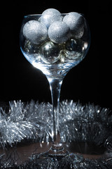 Wine glass filled with Christmas balls. On a black background.