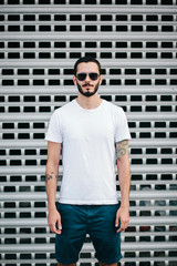 A stylish man with a beard in a white T-shirt and glasses on a city background. Street photo