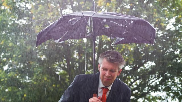Businessman sheltering underneath a broken umbrella in the rain