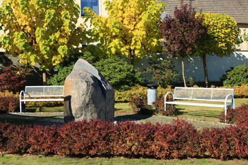 Ławki w parku i ogromny kamień wśród kolorowych jesiennych liści.