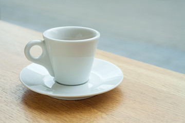 A coffee cup on a saucer on a table near a window