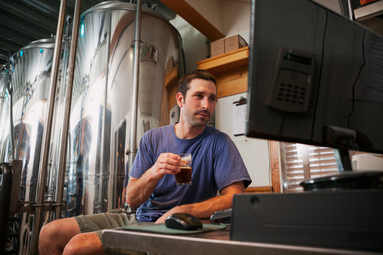 Beer: Brewer Tastes Sample While Checking Computer